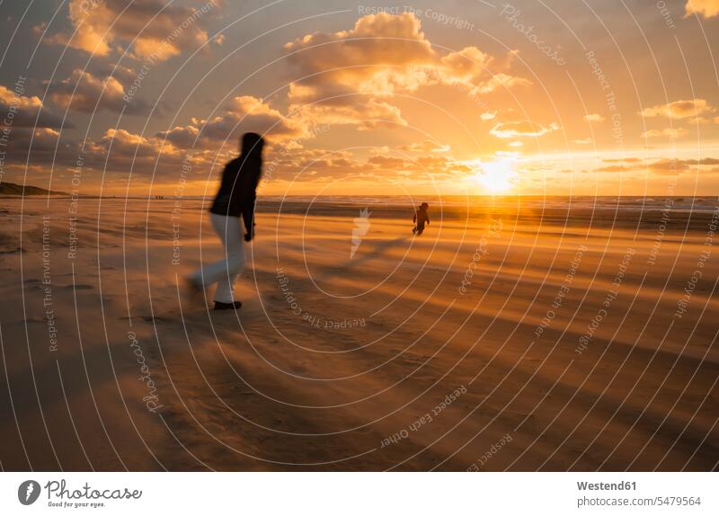 Dänemark, Jütland, Lokken, Mutter versucht, ihr Kind bei Sonnenuntergang am stürmischen Strand zu fangen Lökken Sturm Stuerme Stürme stuermisch