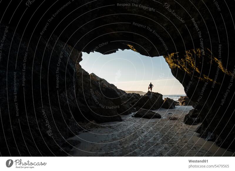 Silhouette eines Mannes, der oben auf den Felsen am Eingang einer leeren Strandhöhle steht Innenaufnahme Innenaufnahmen innen drinnen Abenddämmerung Dämmerung