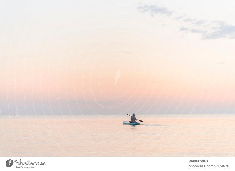 Junge mit Ruder Paddleboarding auf dem Meer bei Sonnenuntergang Farbaufnahme Farbe Farbfoto Farbphoto Außenaufnahme außen draußen im Freien Sonnenuntergänge