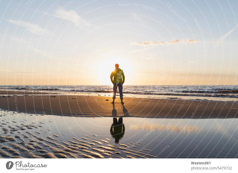 Älterer Mann in voller Länge steht bei Sonnenuntergang am Strand am Ufer, Nordseeküste, Flandern, Belgien Farbaufnahme Farbe Farbfoto Farbphoto Außenaufnahme