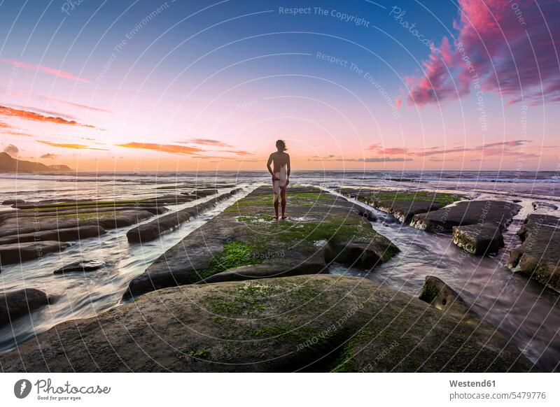Neuseeland, Nordinsel, Rückansicht eines nackten Mannes mit Blick auf das Meer bei Sonnenuntergang Außenaufnahme außen draußen im Freien Sonnenuntergänge