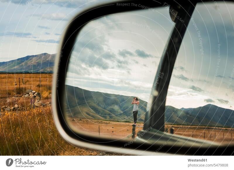 Seitenspiegelreflexion eines jungen Mannes, der auf einem Zaun steht und durch ein Fernglas auf die umliegenden Berge schaut Außenaufnahme außen draußen