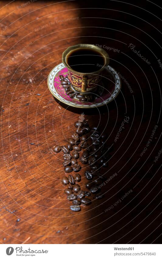 Tasse Kaffee und rohe Kaffeebohnen liegen auf schattigen Tisch dunkel Schatten Kaffeetasse Kaffeetassen Tassen Geschirr geröstete Kaffeebohne