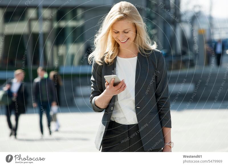 Porträt einer lächelnden blonden Geschäftsfrau, die auf ein Handy schaut Geschäftsfrauen Businesswomen Businessfrauen Businesswoman Smartphone iPhone