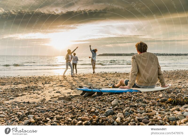 Junger Mann auf dem Surfbrett beobachtet Freunde beim Seifenblasenmachen am Strand bei Sonnenuntergang glücklich Glück glücklich sein glücklichsein entspannt
