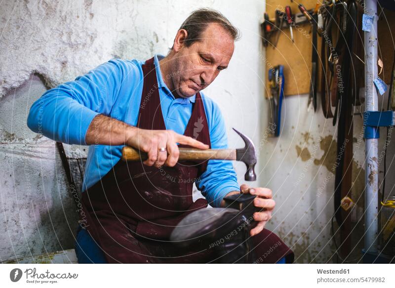 Schuhmacher bei der Reparatur eines Schuhs in seiner Werkstatt Europäer Kaukasier Europäisch kaukasisch Hammer Haemmer Hämmer schlagen Schlag arbeiten Arbeit