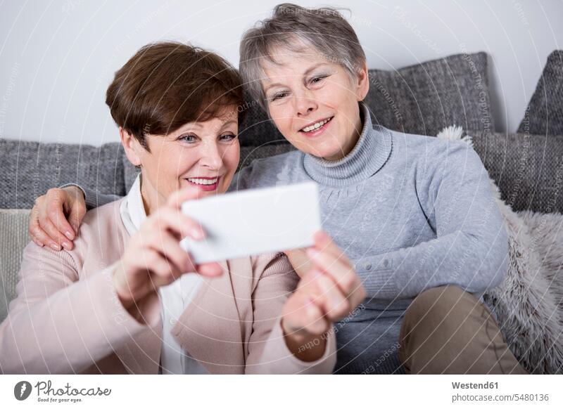 Zwei ältere Frauen sitzen auf der Couch und machen Selfies von sich Freundinnen Gemeinsam Zusammen Miteinander Seniorin Seniorinnen alt sitzend sitzt