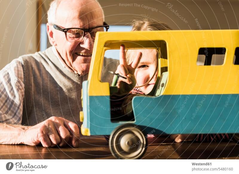 Grossvater und Enkelin bauen Spielzeugbus zusammen, Mädchen macht Siegeszeichen spielen Großvater Opa Großpapa Großpapas Opas Opi Großväter Opis Victory-Zeichen
