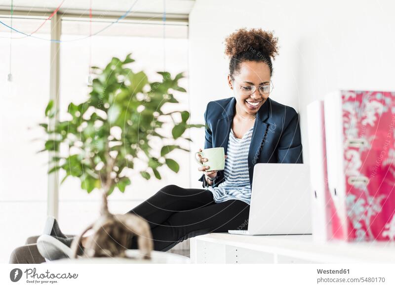 Lächelnde Geschäftsfrau mit Tasse Kaffee schaut auf Laptop Notebook Laptops Notebooks Geschäftsfrauen Businesswomen Businessfrauen Businesswoman Computer