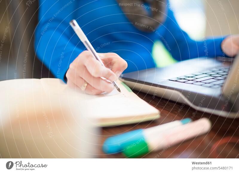 Frau am Schreibtisch mit Laptop beim Schreiben im Notizbuch Notebook Laptops Notebooks weiblich Frauen Notizbücher Notizbuecher schreiben aufschreiben notieren