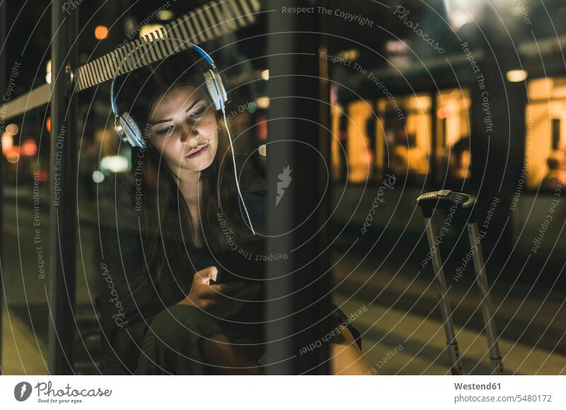 Porträt einer jungen Frau mit Kopfhörern, die nachts auf dem Bahnhof wartet und ein Tablett benutzt Nacht weiblich Frauen Kopfhoerer Erwachsener erwachsen