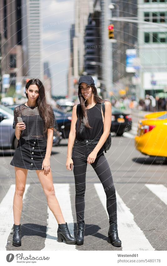 USA, New York City, zwei modische Zwillingsschwestern stehen auf einem Zebrastreifen in Manhattan Schwester Schwestern Freundinnen stehend steht Spaß Spass