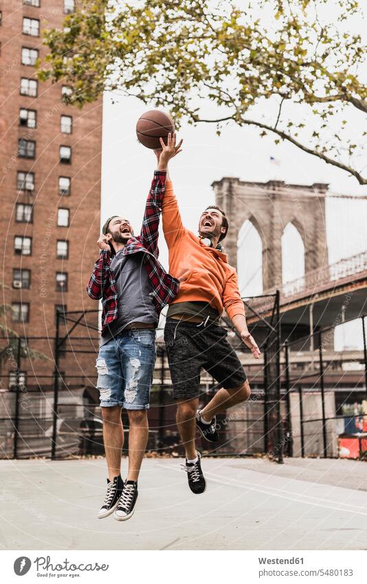 USA, New York, zwei junge Männer spielen Basketball auf einem Aussenplatz Mann männlich springen hüpfen Basketbaelle Basketbälle Freunde Erwachsener erwachsen