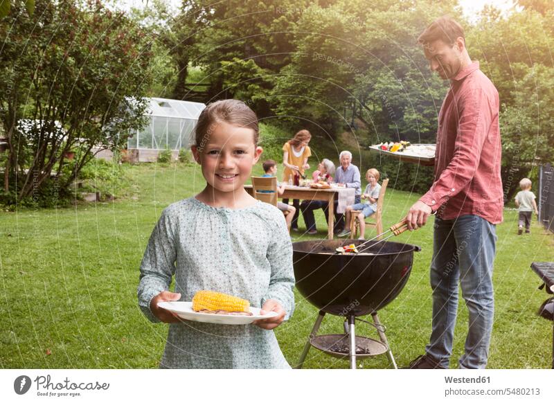 Lächelndes Mädchen hält Teller mit Maiskolben auf einem Familiengrill grillen Garten Gärten Gaerten lächeln Barbecue Grillparties Grillfest Grillen Grillfeste