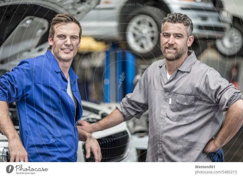 Zwei selbstbewusste Automechaniker in Reparaturwerkstatt lächeln Kollegen Arbeitskollegen Mechaniker Monteur Wagen PKWs Automobil Autos Werkstatt Werkstätte
