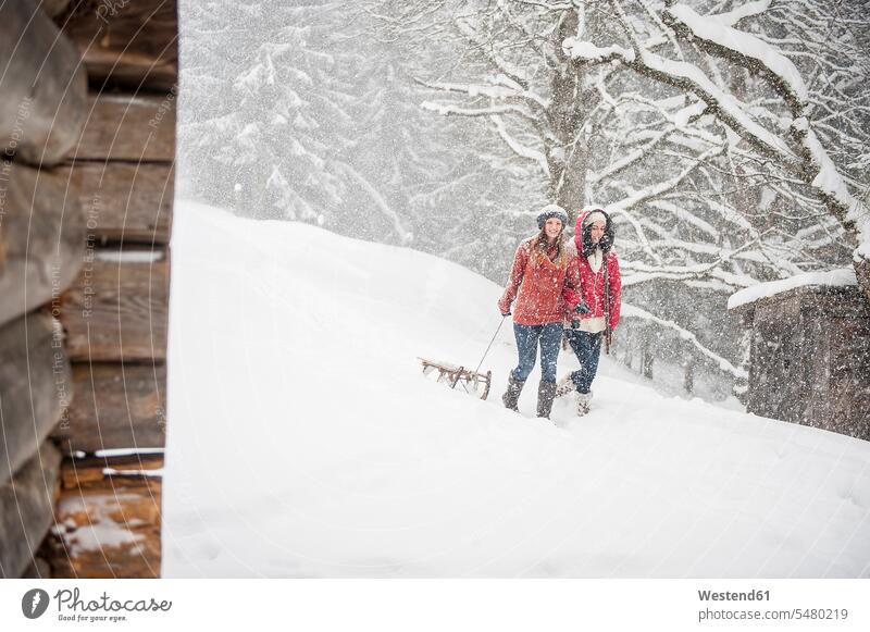 Zwei junge Frauen mit Schlitten bei starkem Schneefall schneien Winter winterlich Winterzeit weiblich Erwachsener erwachsen Mensch Menschen Leute People