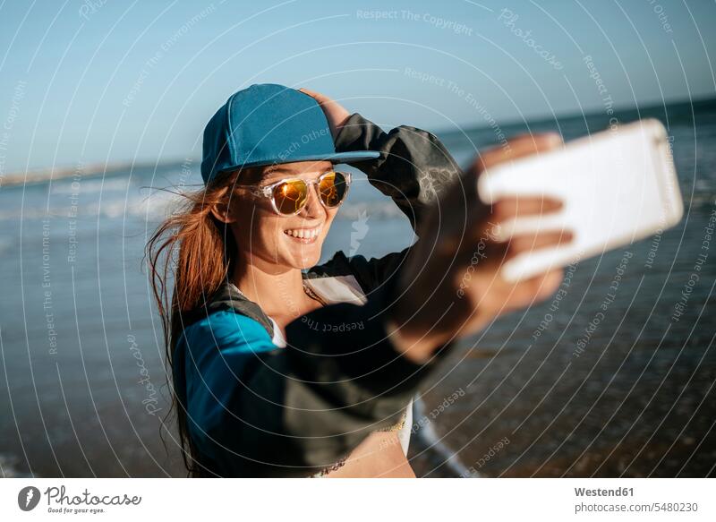 Junge Frau macht ein Selfie am Strand Selfies weiblich Frauen Beach Straende Strände Beaches lächeln fotografieren Erwachsener erwachsen Mensch Menschen Leute