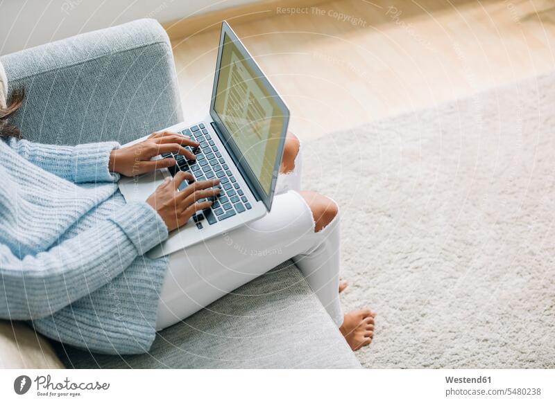 Junge Frau, die zu Hause auf einer Couch sitzt und einen Laptop benutzt, Teilansicht Notebook Laptops Notebooks weiblich Frauen Computer Rechner Erwachsener