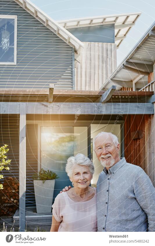 Älteres Ehepaar steht vor ihrem Haus und sieht selbstbewusst aus glücklich Glück glücklich sein glücklichsein Senioren alte ältere stehen stehend Eingang