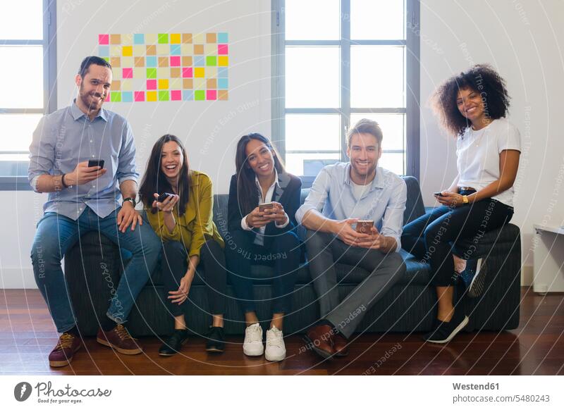 Porträt von glücklichen Kollegen, die mit Mobiltelefonen auf der Couch sitzen Büro Office Büros Arbeitsplatz Arbeitsstätte Arbeitstelle Arbeitskollegen Handy