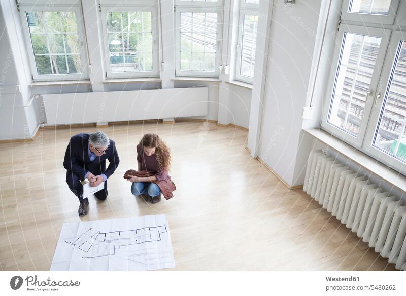 Immobilienmakler zeigt dem Kunden in leerer Wohnung Bauplan Mietwohnungen wohnen erklären erklaeren einziehen Einzug Makler sprechen reden Architekturplan