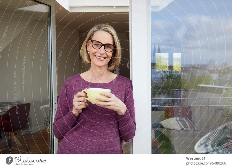 Porträt einer lächelnden reifen Frau mit Kaffeetasse auf dem Balkon Portrait Porträts Portraits Fenster weiblich Frauen Getränk Getraenk Getränke Getraenke