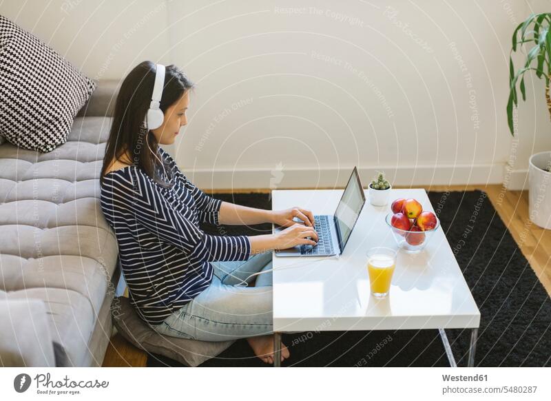 Junge Frau benutzt Laptop und Kopfhörer zu Hause weiblich Frauen Notebook Laptops Notebooks Erwachsener erwachsen Mensch Menschen Leute People Personen Computer