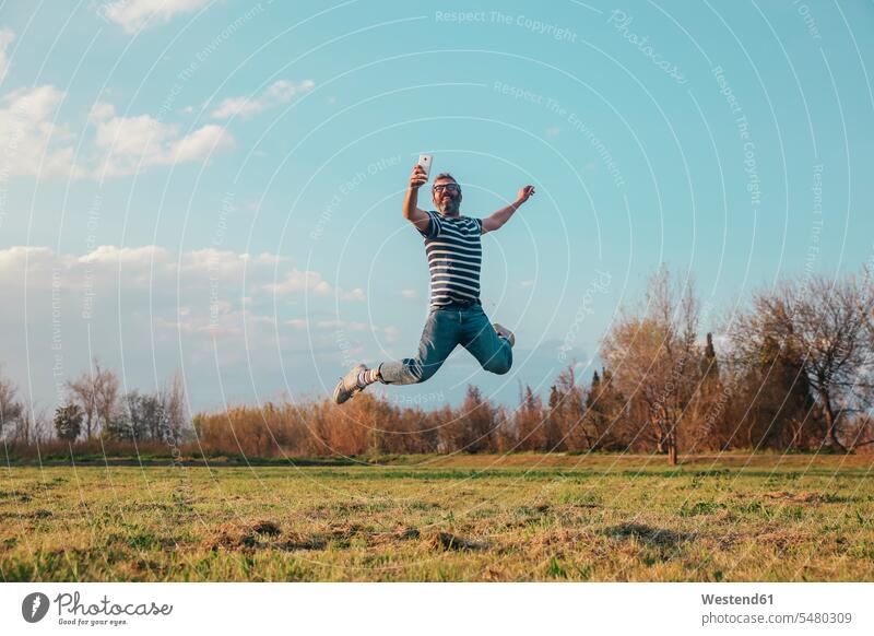 Lächelnder Mann springt in die Luft, während er mit einer Oldtimer-Kamera fotografiert Männer männlich springen hüpfen Selfie Selfies Erwachsener erwachsen