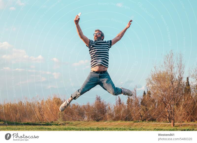 Mann springt in die Luft, während er mit einem Smartphone fotografiert Männer männlich Selfie Selfies springen hüpfen Erwachsener erwachsen Mensch Menschen