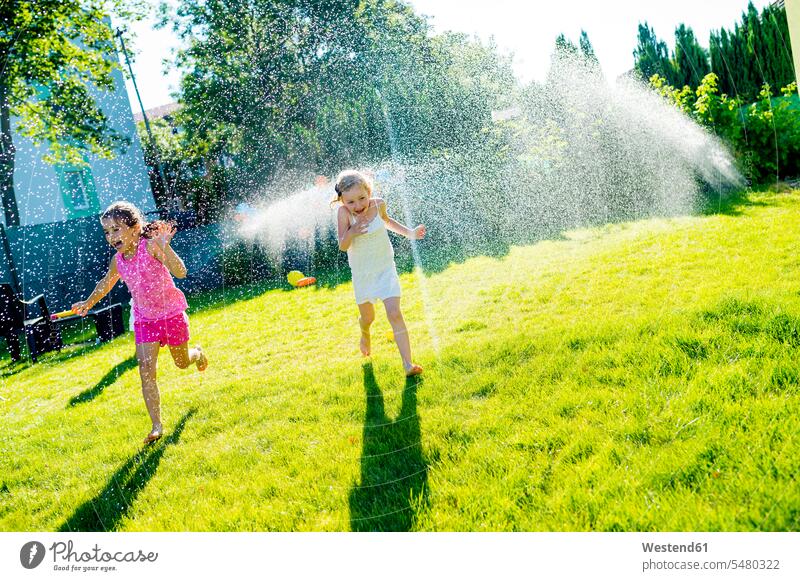 Kinder haben Spaß mit Rasensprenger im Garten Wasser Mädchen weiblich Kids Mensch Menschen Leute People Personen spielen Gärten Gaerten laufen rennen schreien