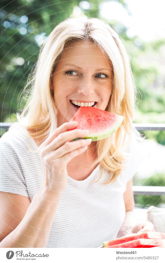 Reife Frau sitzt auf dem Balkon, isst Wassermelone, Porträt weiblich Frauen essen essend Citrullus lanatus Wassermelonen Balkone attraktiv schoen gut aussehend