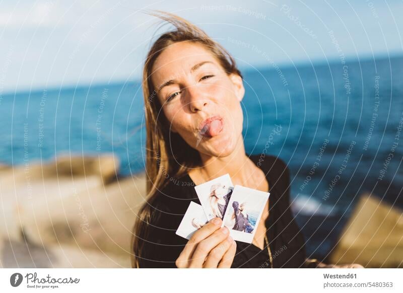 Freche junge Frau zeigt Sofortfotos von sich an der Strandpromenade Foto Fotos zeigen vorführen präsentieren Vorführung herzeigen glücklich Glück glücklich sein