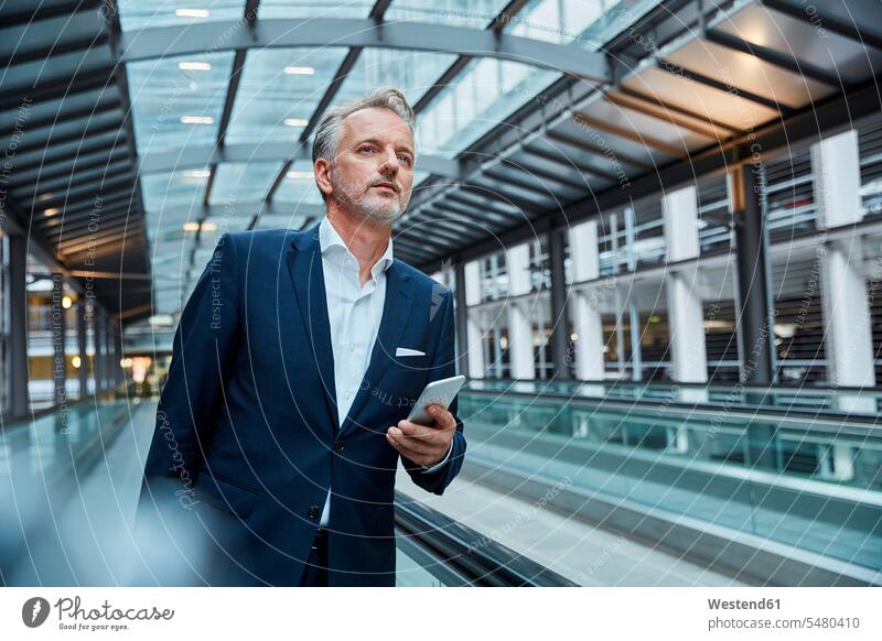 Geschäftsmann mit Smartphone am Flughafen, auf dem Fahrsteig stehend Geschäftsreise Geschaeftsreise Geschäftsreisen Geschaeftsreisen Flughaefen Flugplätze