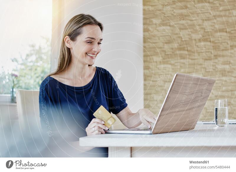 Glückliche Frau beim Online-Shopping zu Hause Kreditkarte EC-Karte Kreditkarten Laptop Notebook Laptops Notebooks lächeln Internet weiblich Frauen glücklich