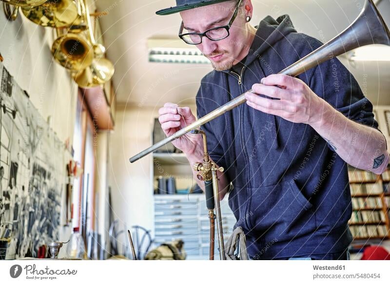 Instrumentenbauer baut Trompete in der Werkstatt Musikinstrumentenbauer Mann Männer männlich bauen Handwerker arbeiten Arbeit Werkstätte Werkstaette