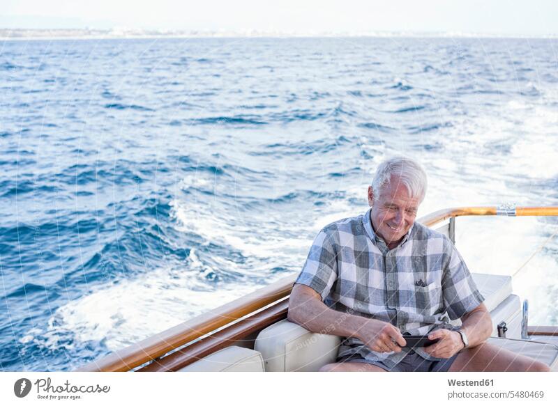 Älterer Mann auf einer Bootsfahrt mit Blick auf Handy Mobiltelefon Handies Handys Mobiltelefone sitzen sitzend sitzt lächeln Männer männlich Boote Telefon