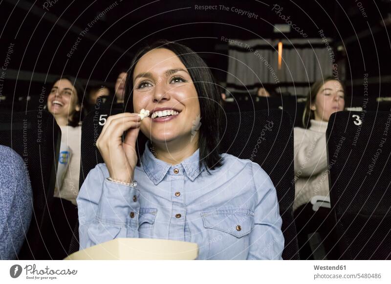 Frau, die sich im Kino einen Film ansieht Kinosaele Kinosaal Kinosäle sitzen sitzend sitzt weiblich Frauen essen essend Zuschauer Publikum Popcorn Puffmais
