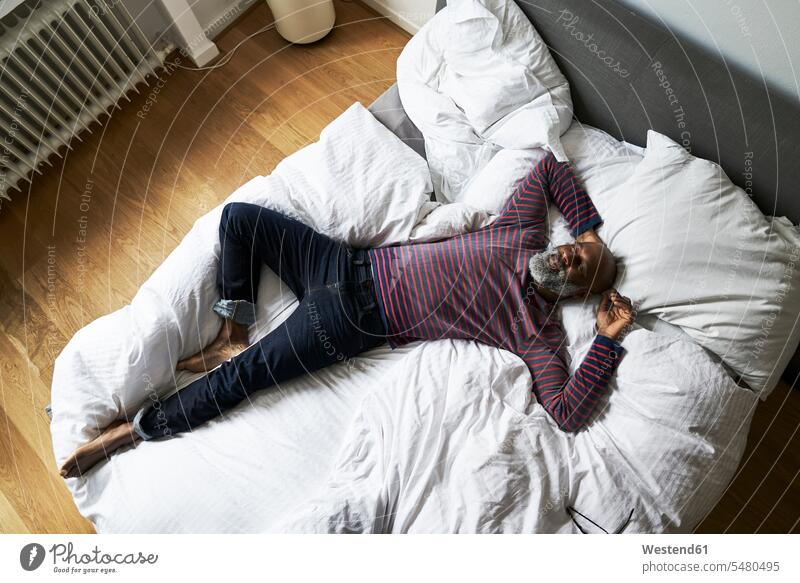 Reifer Mann liegt auf dem Bett und lächelt Betten Männer männlich entspannt entspanntheit relaxt Zuhause zu Hause daheim tagträumen Tagtraum barfuß nackte Füße