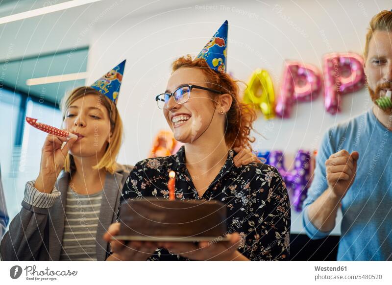 Kollegen mit einer Geburtstagsfeier im Büro mit Kuchen, Partyblower und Partyhüten Feier Fest Festlichkeit Feiern Festlichkeiten Feste Geburtstagsfeiern