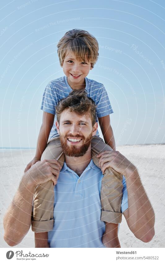 Porträt eines Vaters, der seinen Sohn huckepack am Strand trägt Beach Straende Strände Beaches Söhne lächeln Papas Väter Vati Vatis Papis glücklich Glück