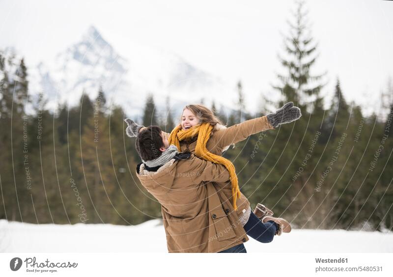 Glückliches junges Paar amüsiert sich in Winterlandschaft Pärchen Paare Partnerschaft Mensch Menschen Leute People Personen lachen hochhalten heben hochheben