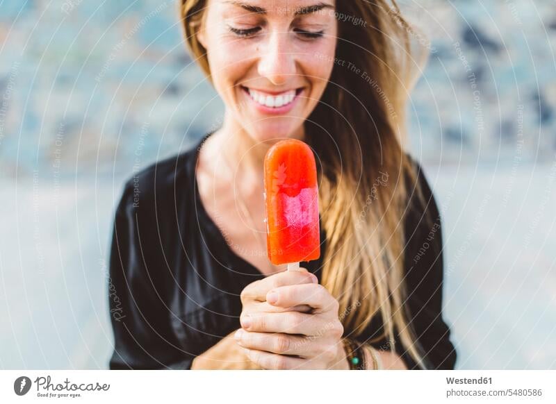 Lächelnde junge Frau hält Eis am Stiel weiblich Frauen Speiseeis glücklich Glück glücklich sein glücklichsein Erwachsener erwachsen Mensch Menschen Leute People