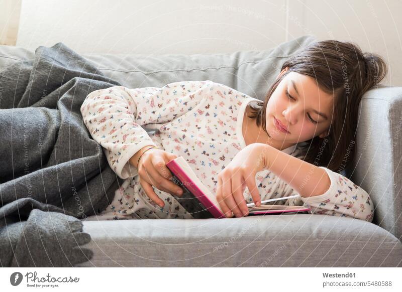 Mädchen liegt auf der Couch und liest ein Buch lesen Kind Mensch Sofa liegen braune Haare konzentriert Decke Vorderansicht Entspannung Seitenlage