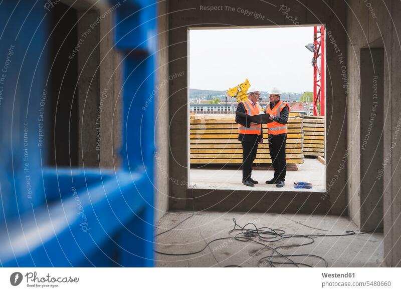 Zwei Männer in Sicherheitswesten unterhalten sich in einem im Bau befindlichen Gebäude arbeiten Arbeit sprechen reden Mann männlich Baustelle Baustellen