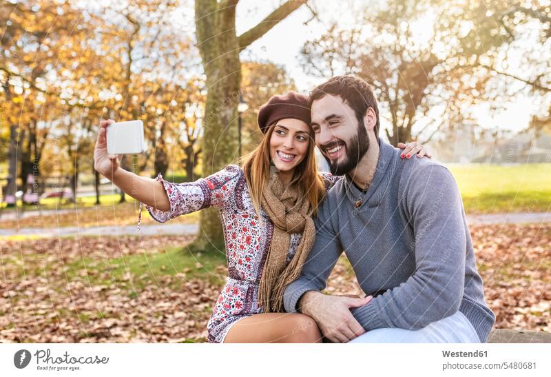 Glückliches Paar macht Selfie mit Smartphone im herbstlichen Park Herbst Pärchen Paare Partnerschaft Selfies Mensch Menschen Leute People Personen iPhone