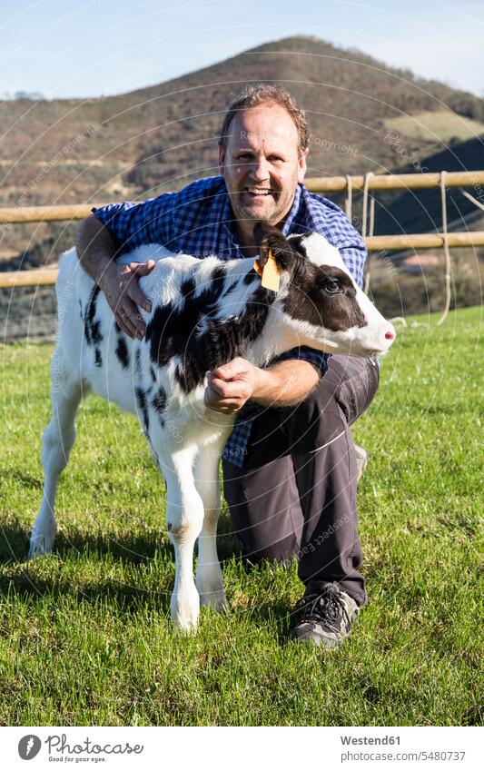 Porträt eines lächelnden Bauern mit Kalb auf der Weide Landwirte Mann Männer männlich Kälber Kaelber Kuh Kühe Kuehe Bauernhof Farmen Bauernhoefe Bauernhöfe