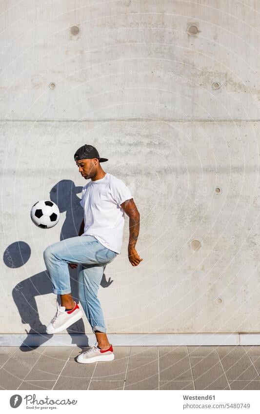 Junger Mann spielt mit Fussball vor einer Betonmauer kicken Fußball Fußbälle Männer männlich Ball Bälle Erwachsener erwachsen Mensch Menschen Leute People