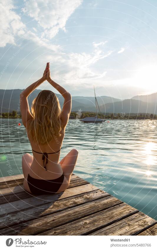 Österreich, Sankt Wolfgang, Frau im Bikini in Yoga-Pose auf dem Steg am See sitzend sitzt Seen Yoga-Übungen Yogauebungen Yogaübungen Jogauebung Jogauebungen