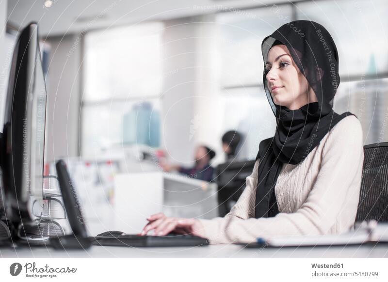 Junge Frau mit Hijab bei der Arbeit am Schreibtisch im Büro weiblich Frauen Office Büros Portrait Porträts Portraits Kopftuch Kopftücher arbeiten Erwachsener
