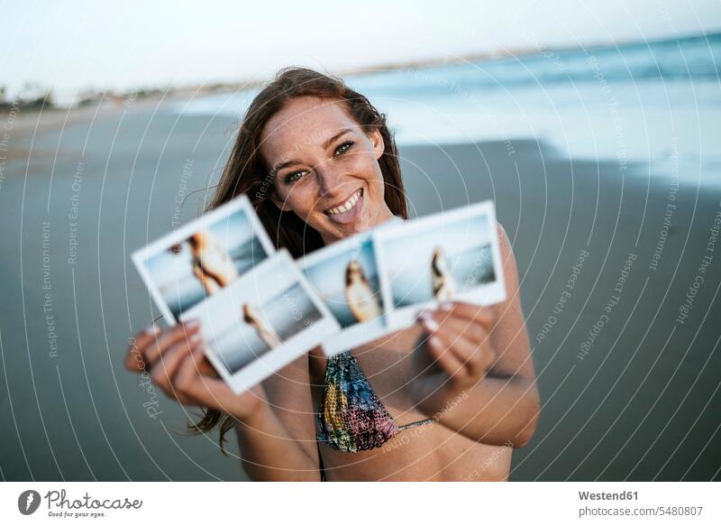 Junge Frau zeigt Sofortfotos am Strand Foto Fotos lächeln weiblich Frauen Beach Straende Strände Beaches Bild Bildnis Bilder Erwachsener erwachsen Mensch